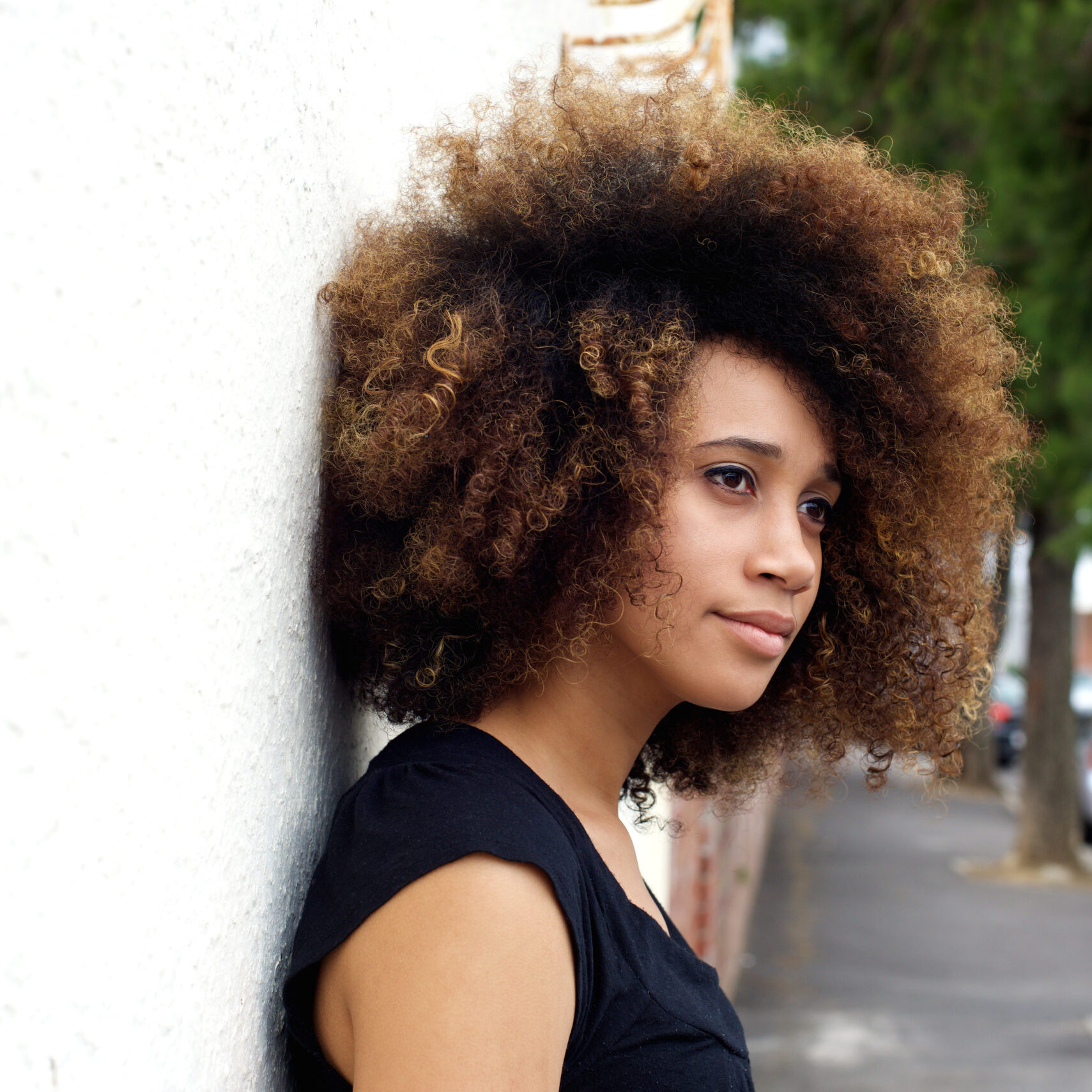 Side portrait of young african american woman leaning against wall and looking away